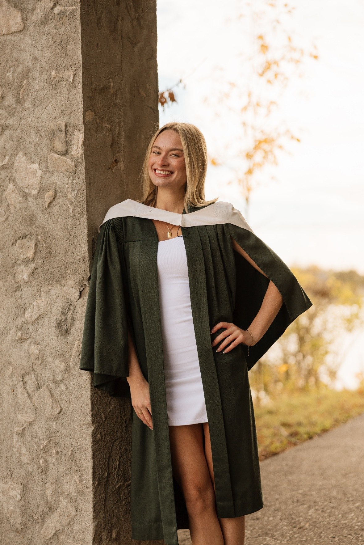 Graduate in her gown leaning against a stone pillar